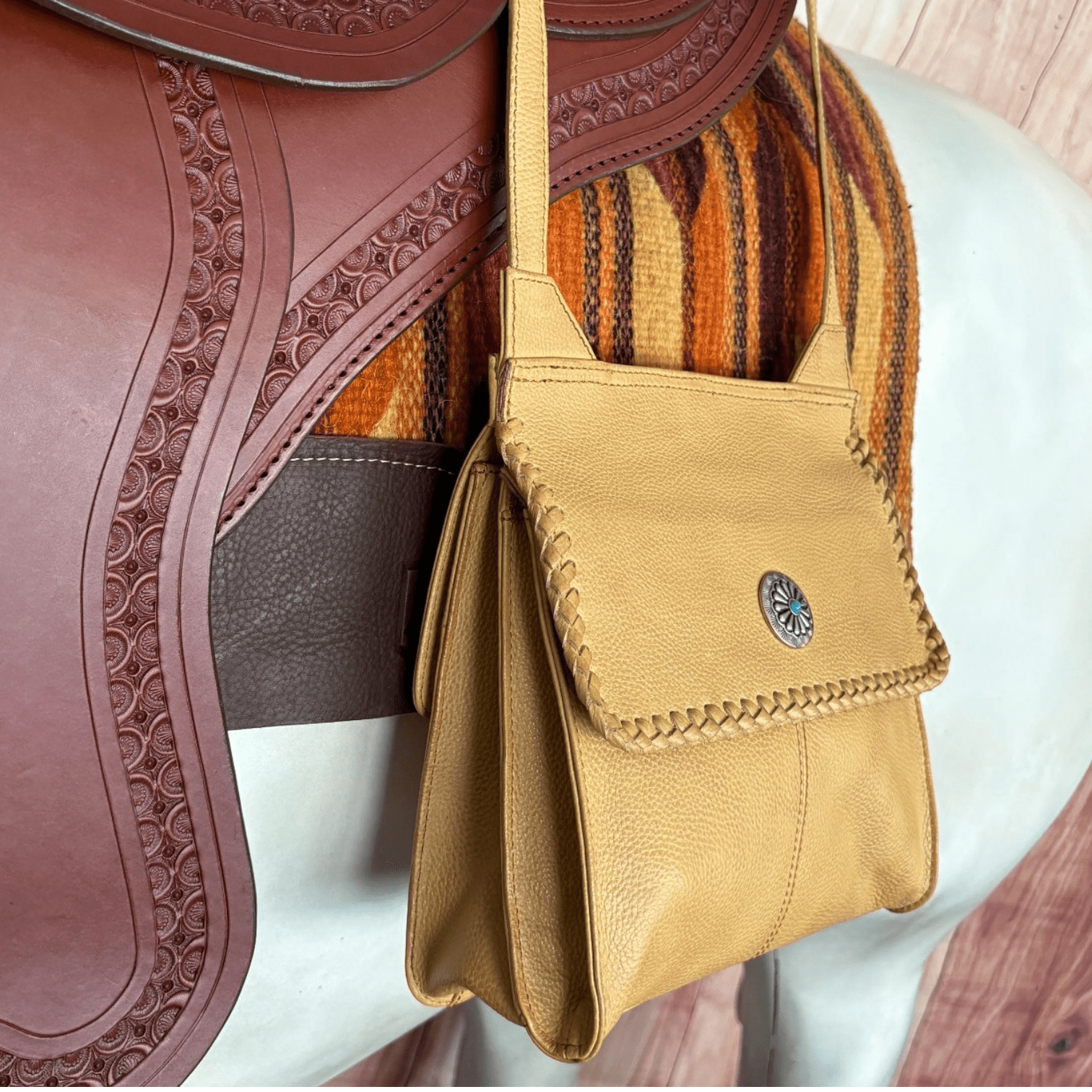 The Golden Mesa Crossbody Purse brings understated Western style to an easy everyday design. Its warm golden-tan finish is accented with beautiful hand-laced detailing around the flap and a small turquoise-inspired concho for a classic Southwestern touch. The adjustable crossbody strap makes it comfortable and convenient to carry, while the compact design keeps your essentials close without sacrificing style. A beautiful choice for adding a little Western character to any outfit.