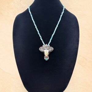 Amazonite Longhorn necklace featuring a carved bone longhorn skull accented with turquoise and ornate Tibetan silver detailing. The pendant is decorated with three silver flowers above the skull and features an intricate floral design on the reverse. The necklace is made with soft mint-green Amazonite beads and silver-toned accents.