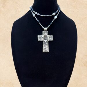 Faith And Flowers necklace featuring an ornate Tibetan silver cross pendant with intricate floral engravings and a raised three-dimensional flower at the center. The reverse side also features decorative detailing. The necklace is adorned with lustrous freshwater pearls and shimmering blue and silver-toned crystal beads, displayed in a beautiful layered style.