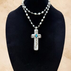 Faith And Pearls necklace featuring a carved bone cross pendant adorned with a genuine turquoise stone and ornate Tibetan silver repoussé-style detailing. The reverse side features an intricate floral pattern. Suspended from a beautiful strand of lustrous freshwater pearls and shimmering faceted crystals with silver-toned links.