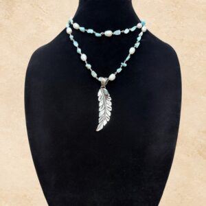 A beautiful blend of Southwestern charm and natural elegance, our Feather And Larimar Necklace combines soft blue Larimar stones with lustrous freshwater pearls for a fresh, feminine look. The centerpiece features an intricately detailed Tibetan silver feather pendant accented with a vibrant turquoise stone. Beautiful decorative detailing on the reverse adds another special touch to this unique piece. The delicate Larimar stones showcase lovely shades of sky blue and soft aqua, beautifully complemented by genuine freshwater pearls and silver-toned links. Designed as one long strand, this versatile necklace can be worn at its full length or doubled for a shorter, layered look. Perfect for adding a touch of Western elegance to everyday outfits or dressing up for a special occasion. A stunning combination of natural Larimar, freshwater pearls, turquoise, and ornate Tibetan silver craftsmanship.