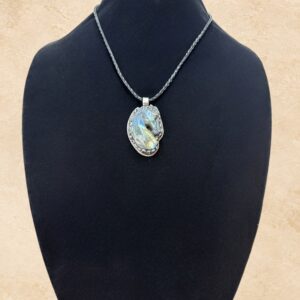 Labradorite Horse necklace featuring a beautifully carved horse head pendant made from genuine Labradorite with shimmering flashes of blue, green, and gold. The pendant is framed in ornate Tibetan silver metalwork with intricate floral detailing on the reverse. Suspended from a braided black leather cord with a convenient magnetic closure.