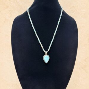 Larimar Teardrop necklace featuring a large, natural sky-blue Larimar gemstone set in an ornate Tibetan silver repoussé-style teardrop pendant with a decorative floral design on the reverse. The necklace features mixed Amazonite beads in soft mint-green, pale turquoise, and creamy white tones with delicate silver-toned accents.